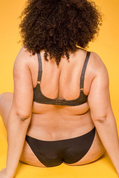 Free Back view of anonymous plus size African American female model in black lingerie sitting on yellow background in light studio Stock Photo