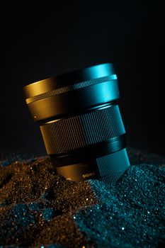 Camera lens partially submerged in sparkly sand with ambient lighting.