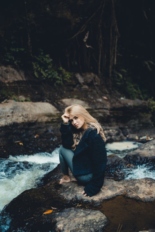 Serene woman sitting on stone near fast river