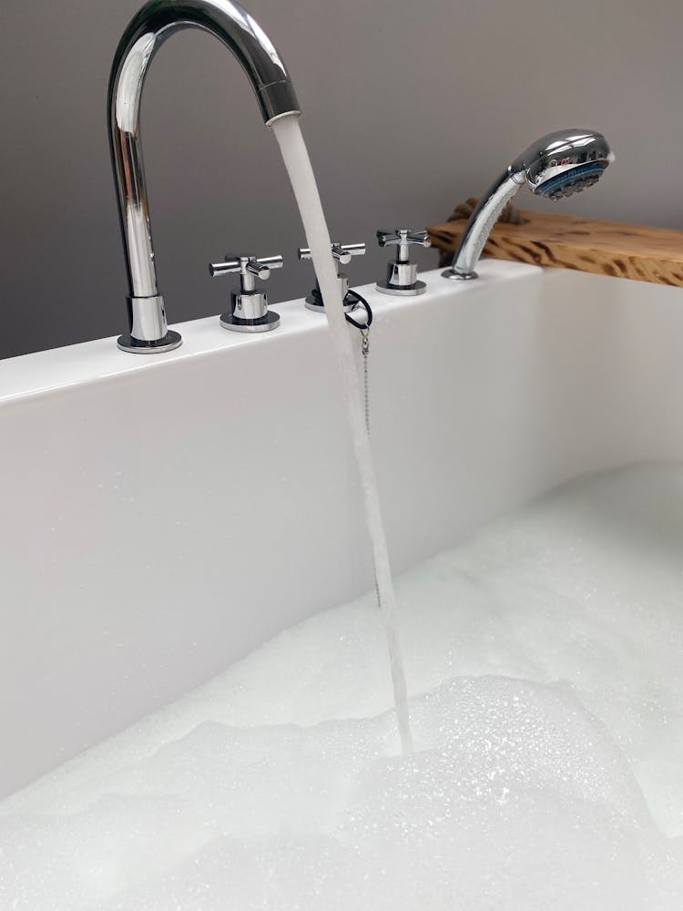 Photo Of A Running Faucet On A White Bathtub