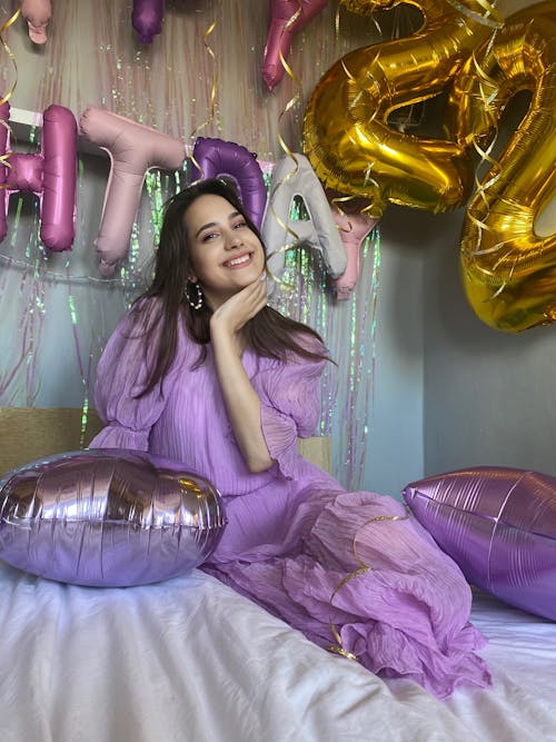 Free A Woman Wearing a Purple Dress and Sitting on a Bed with Balloons Stock Photo