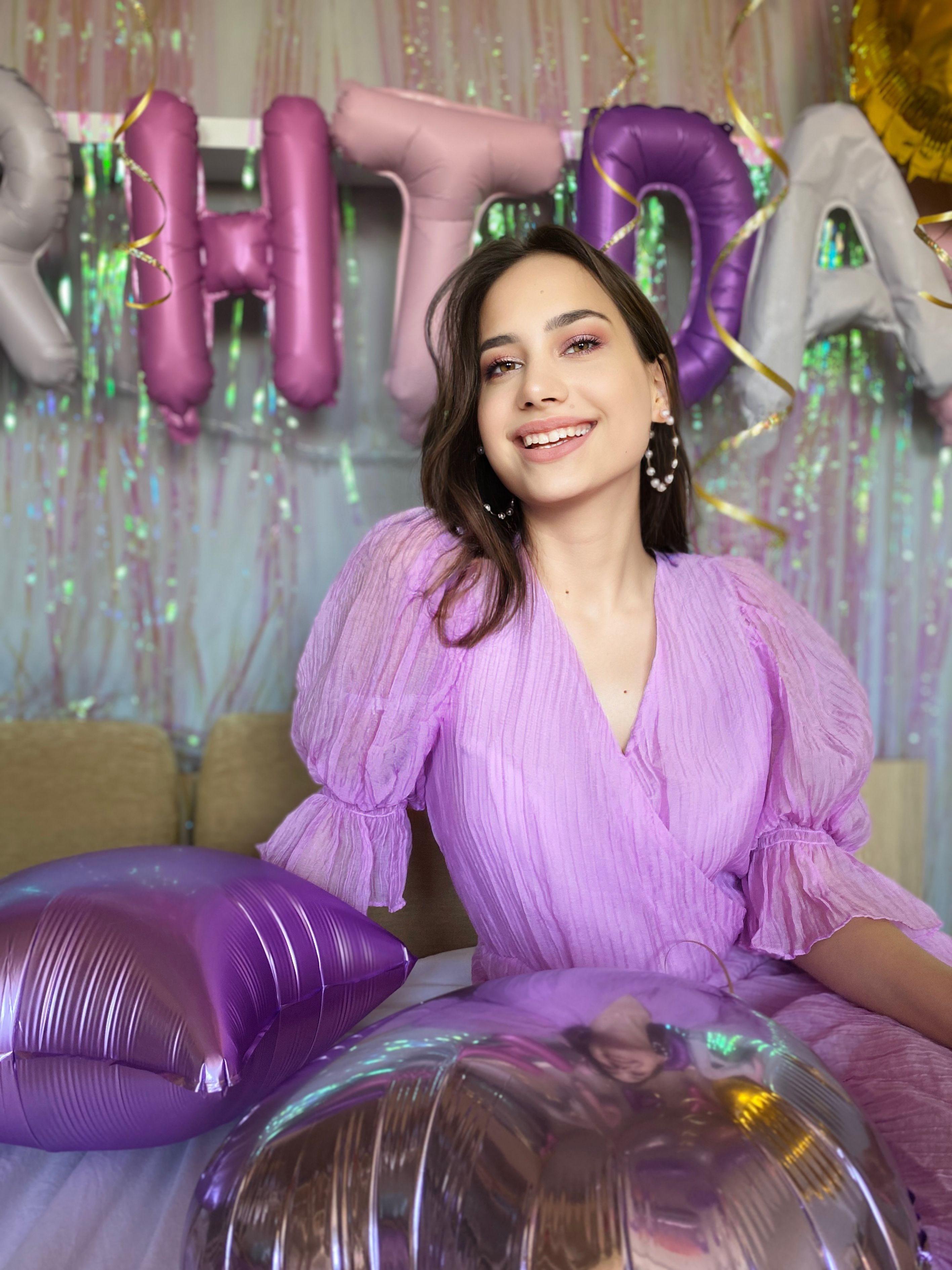 Cheerful woman in a purple dress at a vibrant birthday party with balloons.