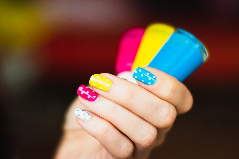 Mano sujetando barras de color con uñas de lunares en amarillo, rosa y azul