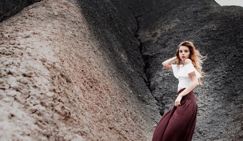 Woman in White Shirt and Maroon Skirt Sitting on Rock