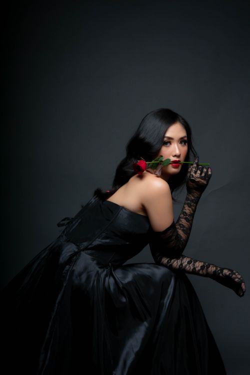 Free Elegant woman in a black dress holding a rose, set against a dark background. Stock Photo