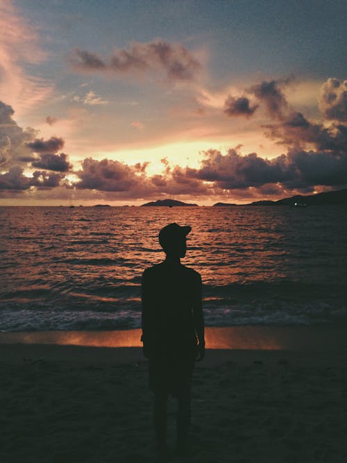 Free A Silhouette of Man Standing on the Beach Stock Photo