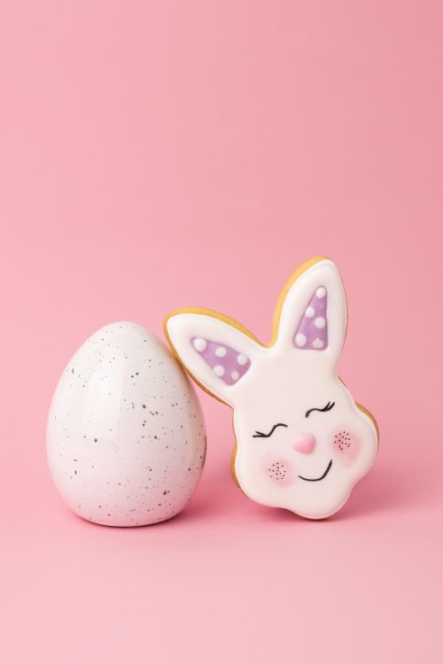 Free Adorable Easter bunny and egg cookies on a pastel pink background, perfect for seasonal decorations. Stock Photo
