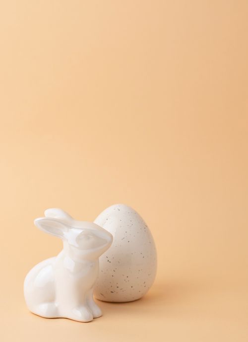 Free Ceramic Easter bunny and egg against a soft peach background, perfect for holiday decoration themes. Stock Photo