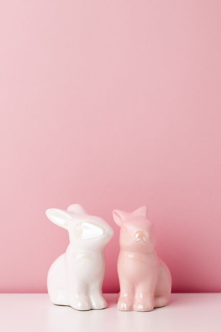 Two pastel ceramic bunny figurines against a pink backdrop, ideal for Easter decor.