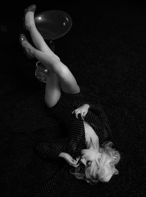 Woman in Polka Dots Dress Lying on the Ground while Legs are Raised on a Chair
