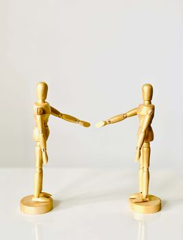 Two wooden mannequins face each other on a white surface, creating a minimalist aesthetic.