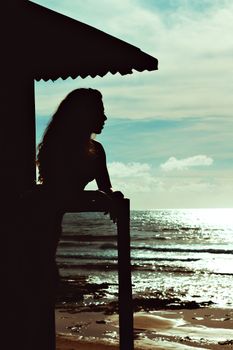 A silhouette of a woman gazing at the ocean from a seaside balcony during sunset.