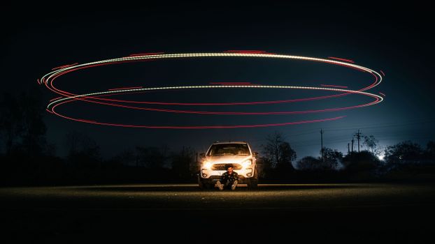 A car with a child seated in front, surrounded by circular light trails in a dark night setting.