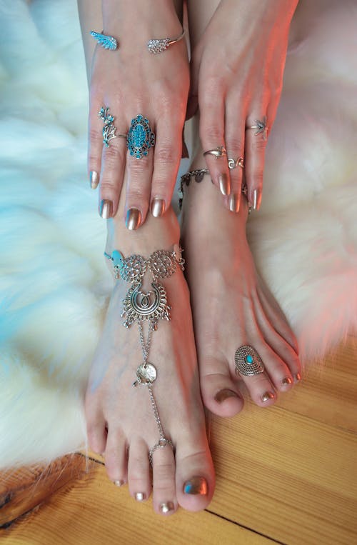 Crop anonymous female with manicured hands in rings touching legs in silver anklets above white carpet