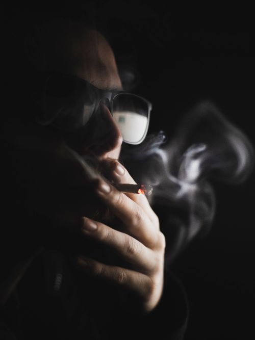 Free Dark, atmospheric portrait of a person smoking a cigarette against a black background. Stock Photo