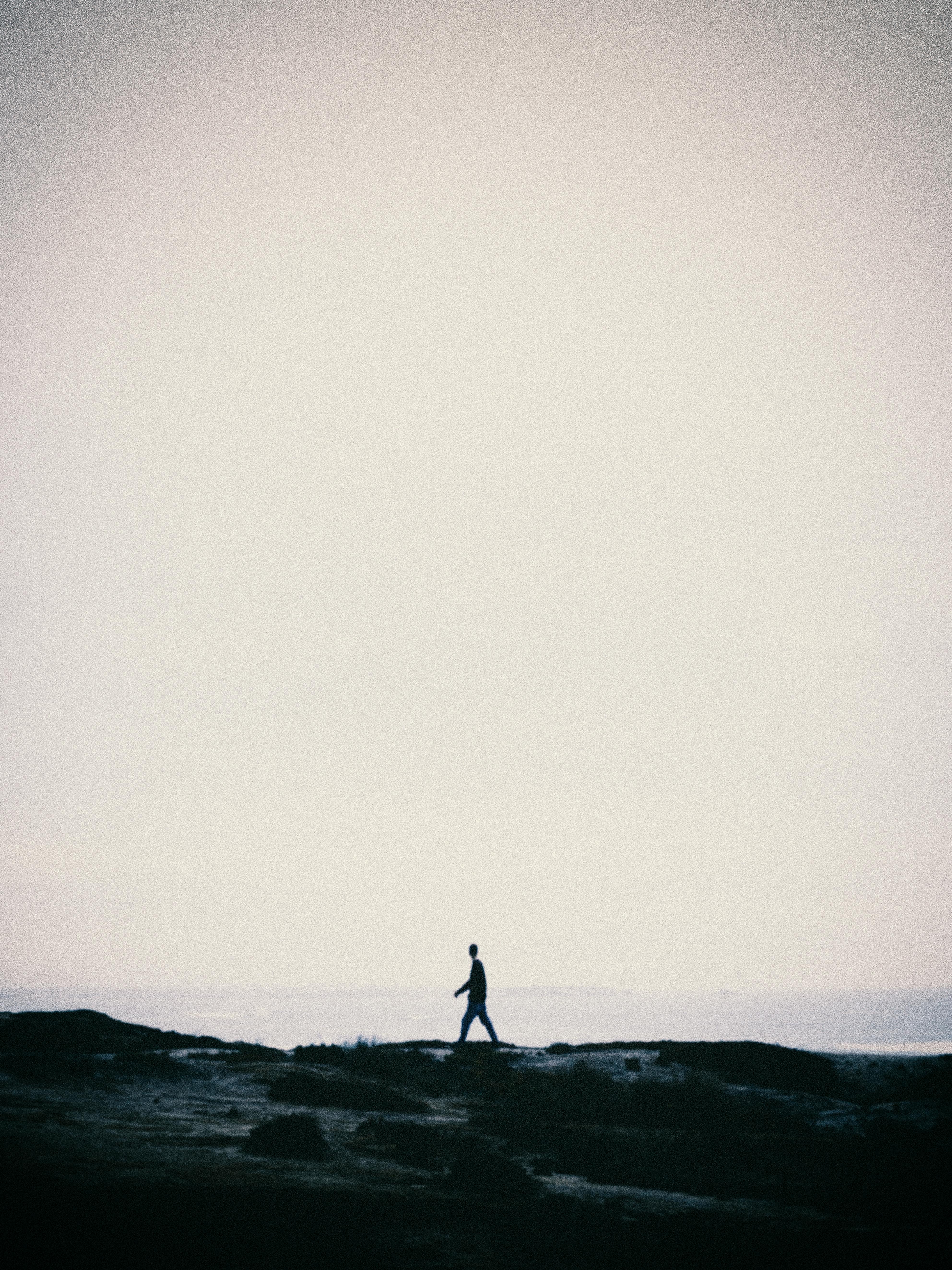 A lone figure walks along a cliff edge, silhouetted against a vast, empty sky, evoking solitude and contemplation.