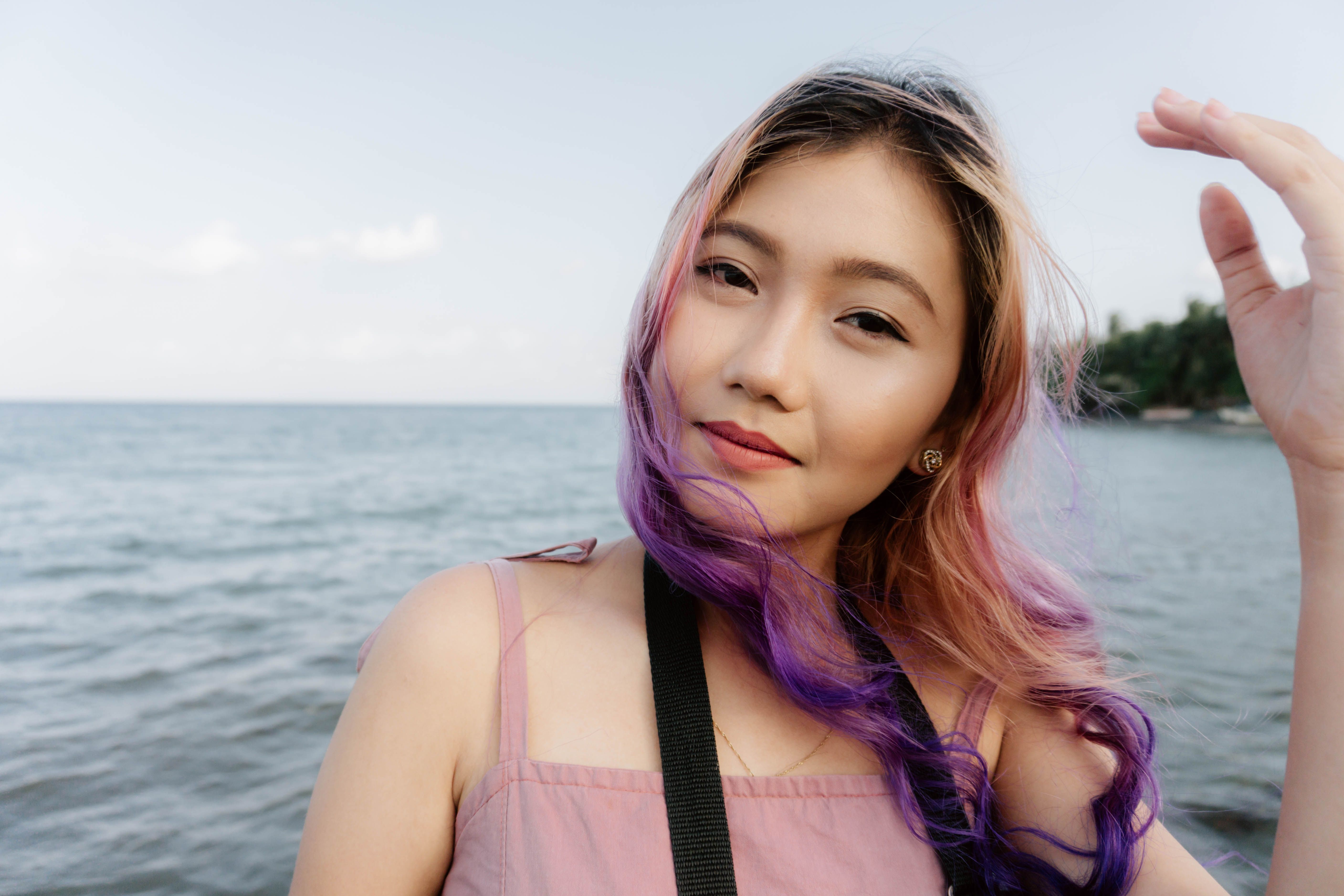 A serene portrait of an Asian woman with colored hair standing by the sea, capturing a tranquil moment outdoors.