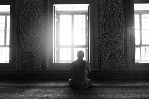 Free Man sitting in contemplation by a window in a richly patterned monochrome interior. Stock Photo