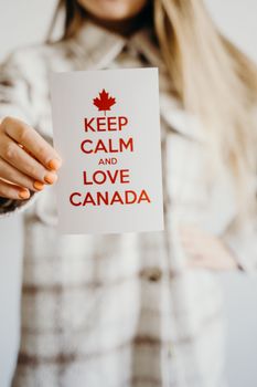 A card with 'Keep Calm and Love Canada' message held by a person in a plaid shirt.