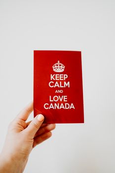 A hand holds a red card with the text 'Keep Calm and Love Canada' against a white background, celebrating Canadian pride.