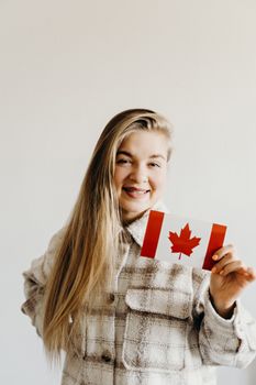 Woman with long blonde hair smiling while holding a small Canadian flag indoors.