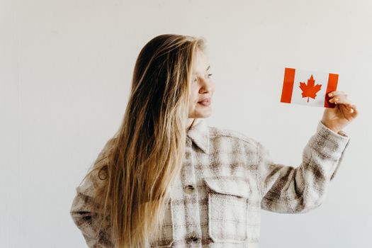Adult woman in plaid coat holding a small Canadian flag against a white background.