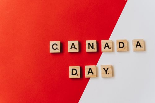 Free Top view of Canada Day text spelled out with wooden letter tiles of board game arranged on red and white surface Stock Photo