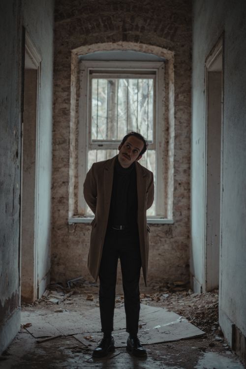 Free Full body of serious male bankrupt wearing elegant outfit standing in corridor of abandoned building with shabby walls and window Stock Photo