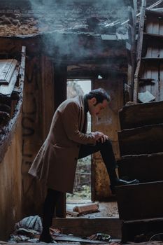 Full body side view of serious male in trendy outfit standing in ruined dirty building with demolished walls and roof