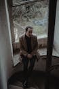 Stylish man sitting near stairway in abandoned house