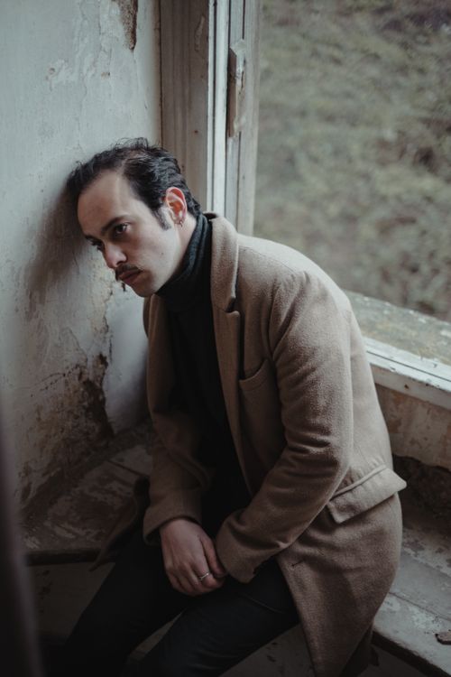 Free Unhappy bankrupt male with mustache in stylish outfit sitting on windowsill near window and shabby wall in abandoned dirty building Stock Photo