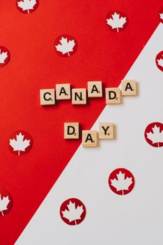 Stylized Canada Day image with maple leaf confetti and Scrabble tiles on red and white background.