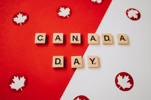 Free Canada Day themed image with scrabble pieces spelling 'Canada Day' and maple leaves on a red and white background. Stock Photo