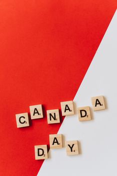 Wooden Scrabble tiles spell Canada Day on a red and white background.