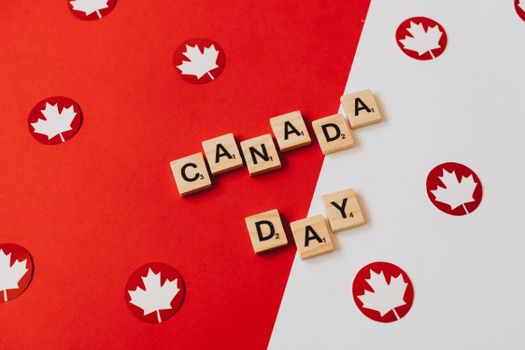 Scrabble tiles spelling 'Canada Day' on a red and white maple leaf background.