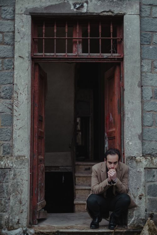 Free Full body of desperate male sitting in doorway of weathered building and feeling hopeless Stock Photo