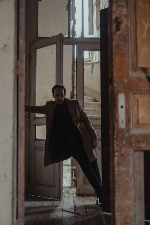 Free Full body of fashionable male in coat standing against shabby opened door of neglected building Stock Photo
