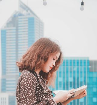 A young woman with curly hair engrossed in a book against a city skyline backdrop.