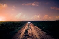 宁静的乡村日落中，一辆白色汽车行驶在田野环绕的土路上