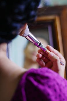 A close-up of a woman applying makeup with a brush in front of a mirror.