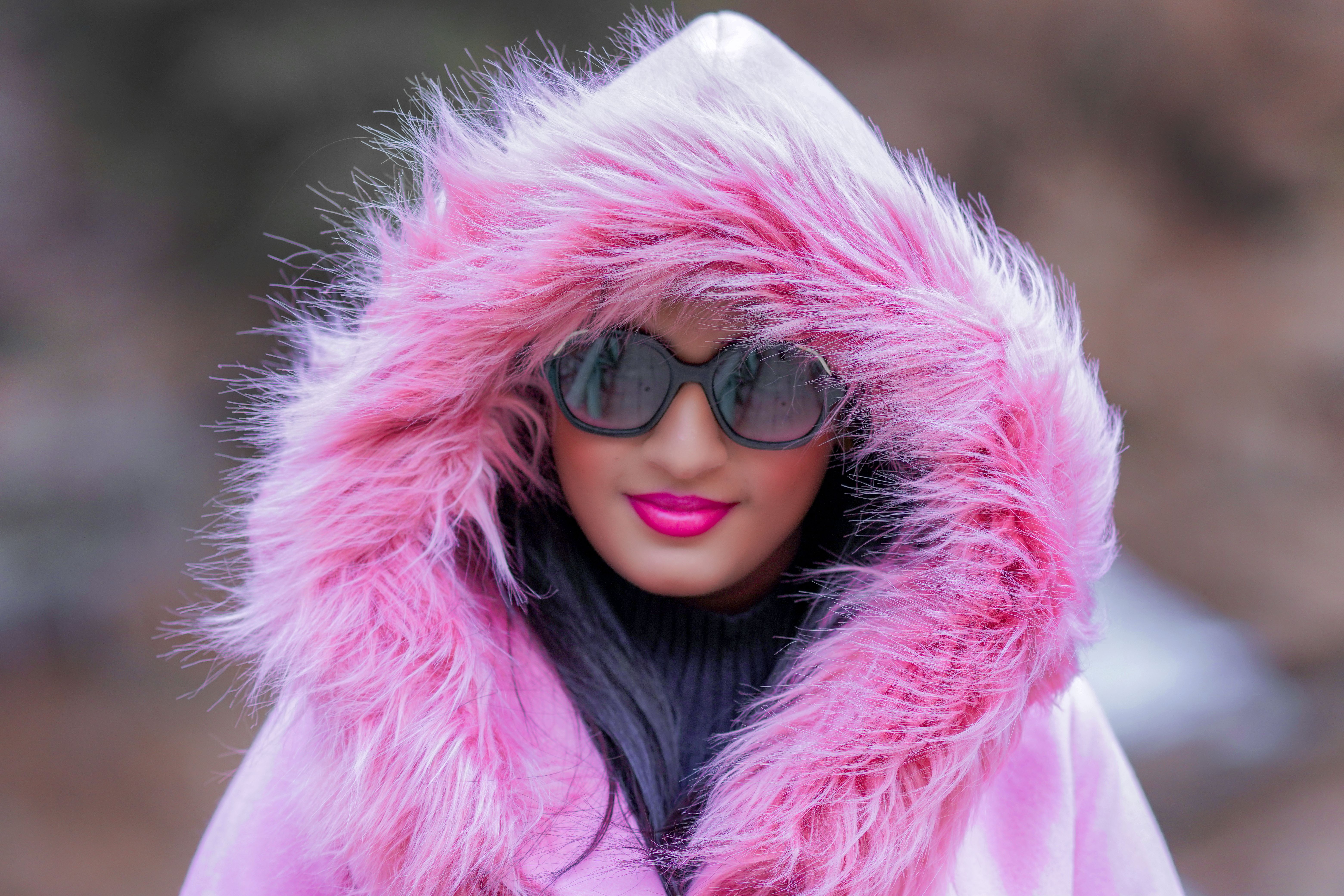 Close-up of a woman wearing a pink fur coat and sunglasses outdoors.