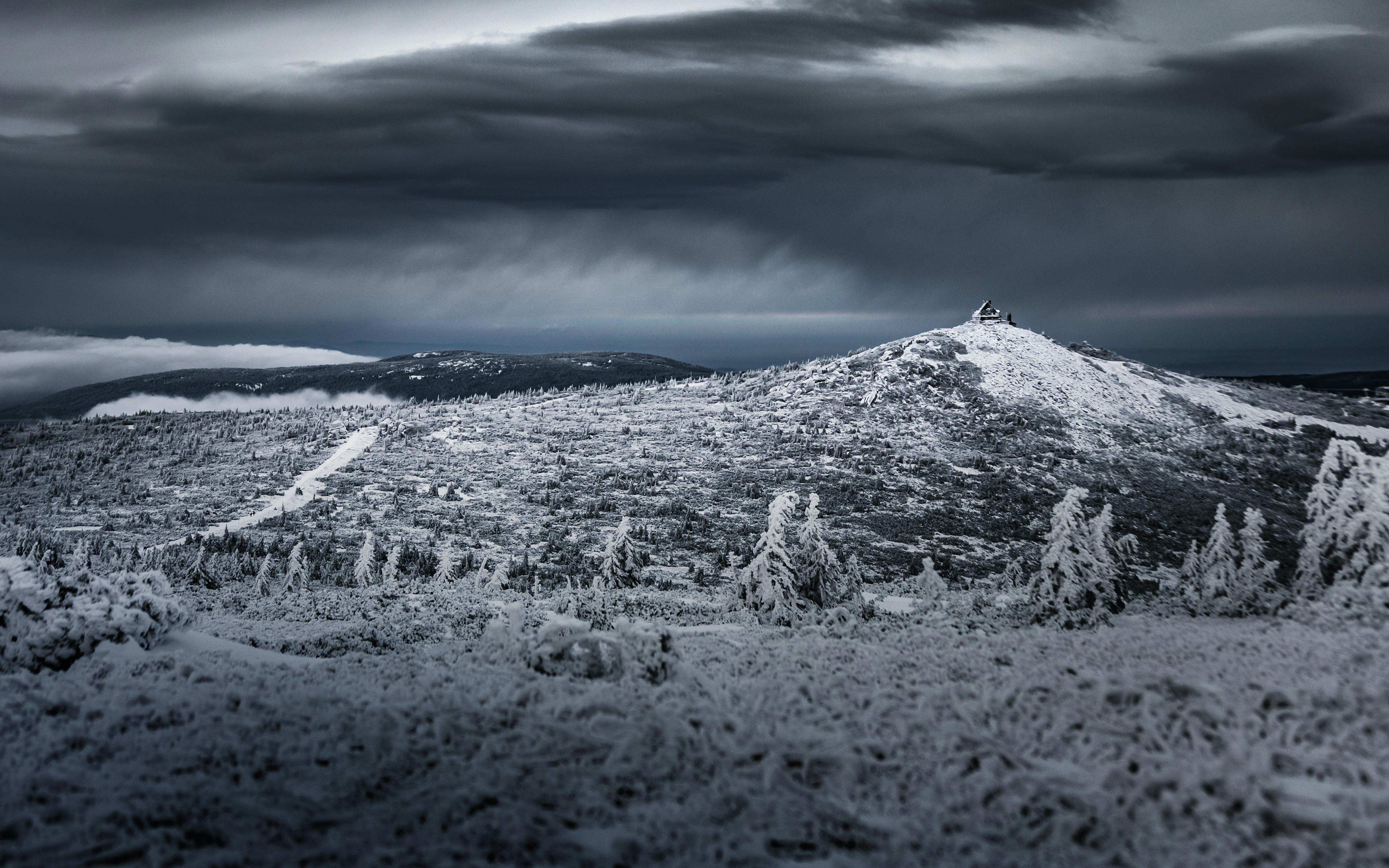 A dramatic view of snow-covered Polish mountains under dark, cloudy skies, capturing the winter wilderness.