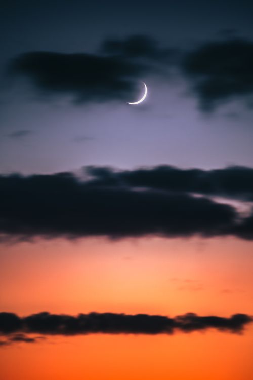 Free Crescent moon in a dramatic twilight sky over dark cloud layers, creating a serene and atmospheric scene. Stock Photo
