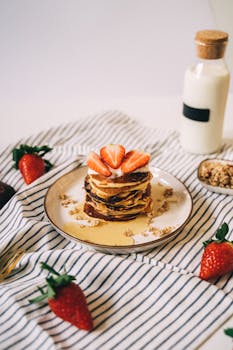 Pancakes topped with strawberries and syrup served on a striped cloth for a perfect breakfast.