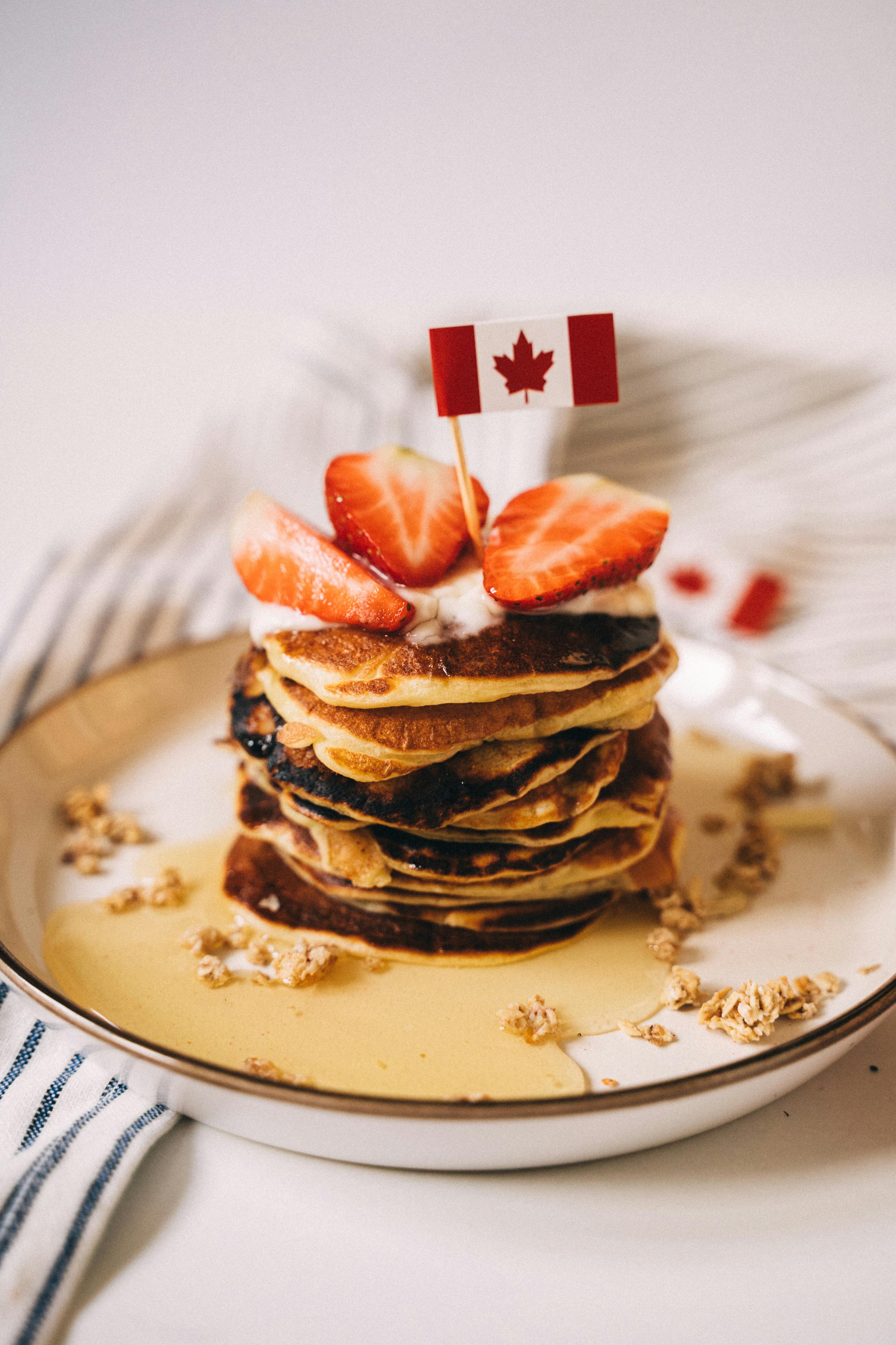 Stack of pancakes with maple syrup and strawberries topped with a Canadian flag.
