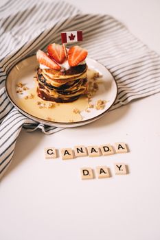 Stack of pancakes with strawberries and syrup, celebrating Canada Day with scrabble tiles.