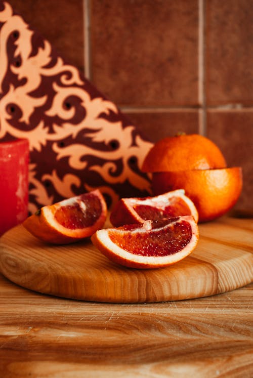 Ripe cut red oranges placed on wooden cutting board near aroma candle near tiled wall