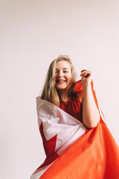 Smiling woman wrapped in Canadian flag with a white background, symbolizing celebration and patriotism.