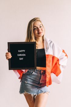 Woman holding a Canada Day sign wrapped in Canadian flag, celebrating indoors.
