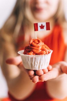 Close-up of a cupcake with a Canadian flag held in hands, symbolizing celebration.
